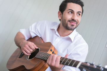 Obraz premium Happy man playing guitar while sitting on sofa in living room, Enjoying carefree time at home.