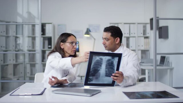 Sequence of shots footage of two modern doctors looking at lungs x-ray and discussing health state of patient