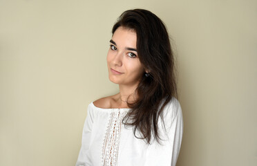 Portrait of young 25 y.o. brunette Russian woman with long hair. In white open shoulder top and looking into the camera on light gray background. Minimum makeup, natural hairstyle. copy space