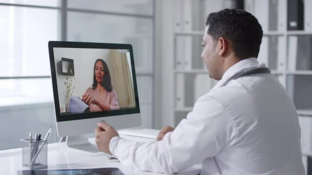 Sequence of shots of modern doctor instructing his patient how to measure blood pressure using tonometer while having video call with her