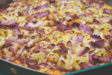 Close up hot fresh-baked Hawaiian pizza cheese melted in carton box on the table at the home background. Enjoying the menu takes away junk food. Fast food takeout delivery.