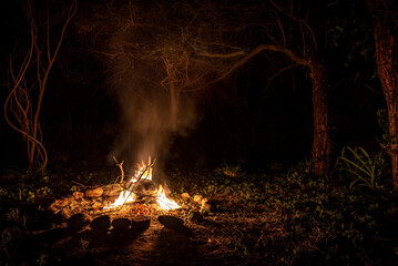 Flames of a campfire at night in a dark spooky forest surrounded by stones shaping strong shadows