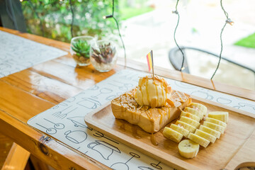 Crispy honey toast caramel with vanilla ice cream and bananas in wooden plate in the cafe. Bread fried sweet butter on the table near wall background by front view. Breakfast gourmet food.