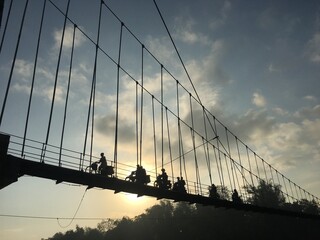 silhouettes of villagers crossing a suspension bridge