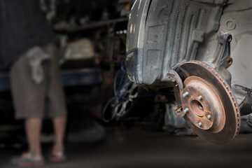 Close-up rusty disk break and wheel hub of 4x4 car waiting check list for repair or maintenance with low light blurry mechanical fitter working in the garage shop background.