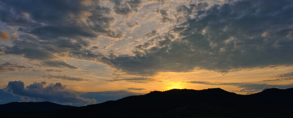 Silhouette of mountains against the background of the shining sun with beautiful clouds