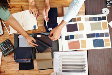 Tailors checking catalog when choosing fabric, zipper and lining fabric for jacket, view from the...