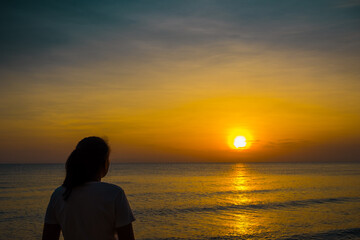 Woman standing in the sea and watching the sunrise. Sunrise silhouette.