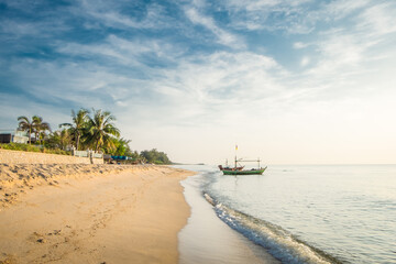 Beautiful view of the turquoise waves with the blue sky and white clouds and fisherman's boat on sandy beach on vacation in Hua Hin, Prachuap Khiri Khan Province, Thailand.
