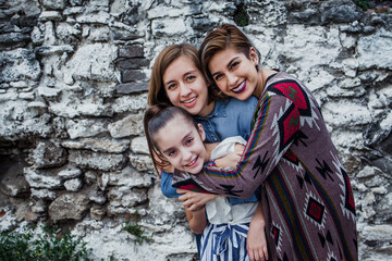 Obraz na płótnie Canvas Portrait of three cheerful Mexican sisters hugging and looking at camera in Latin America