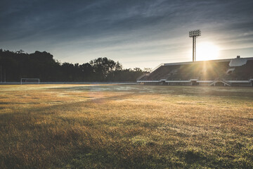Beautiful sunset over the sport field in stadium. Football arena with green grass and rays of sunlight. Soccer tournament background concept.