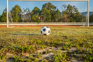 View of classic leather soccer ball on goal net in green grass field the arena stadium. Traditional black and white football equipment to play competitive game. Sports tournament concept.