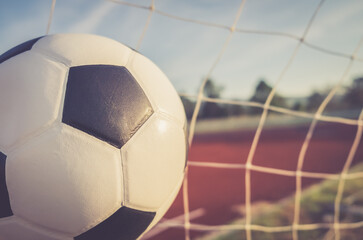 Naklejka premium View of classic leather soccer ball in goal net on blue sky nature background. Traditional black and white football equipment to play competitive game sport tournament concept.