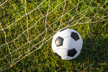 View of classic leather soccer ball on goal net in green grass field the arena stadium. Traditional black and white football equipment to play competitive game. Sports tournament concept. 