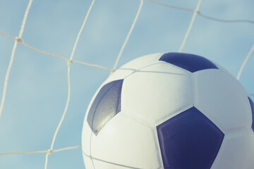 View of classic leather soccer ball in goal net on blue sky nature background. Traditional black and white football equipment to play competitive game sport tournament concept.