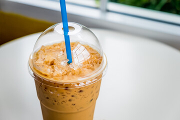 Iced coffee in a plastic cup on a wooden table at the cafe. Cold espresso in the coffee shop with...
