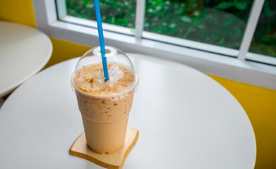 Iced coffee in a plastic cup on a wooden table at the cafe. Cold espresso in the coffee shop with...