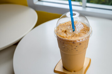 Iced coffee in a plastic cup on a wooden table at the cafe. Cold espresso in the coffee shop with...