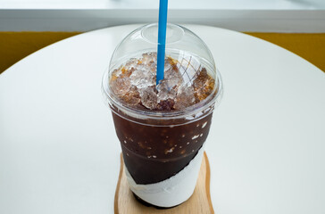 Iced coffee in a plastic cup on a wooden table at the cafe. Cold espresso in the coffee shop. Beverage glass frozen in the restaurant. Food sales busy interior decoration vintage.
