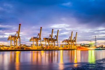 Fototapeta premium Harbor with anchored ship. Container cargo freight ship with working crane bridge at a shipyard in for logistic transportation import and export at Asia haven port background, Samutprakarn, Thailand.