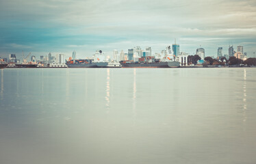 Naklejka premium Harbor with anchored ship. Container cargo freight ship with working crane bridge at a shipyard in for logistic transportation import and export at Asia haven port background, Samutprakarn, Thailand.