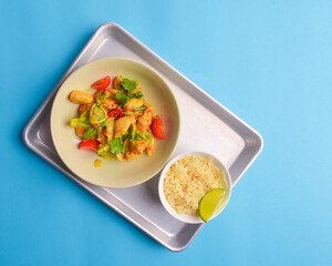 Fresh rice and chicken in gravy sauce with tomatoes, red pepper and green beans served in seperate plates on metal tray.