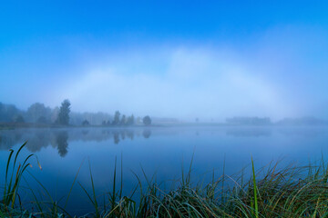 Fototapeta na wymiar unusual natural phenomenon with a rainbow of fog over the lake, blurred misty landscape in the morning, blurred background