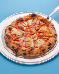 Whole Italian pizza with cheese and mushrooms on a metal tray over bright blue pastel bakcground.