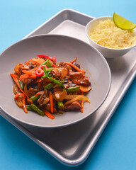 Fresh rice and chicken in gravy sauce with tomatoes, red pepper and green beans served in seperate plates on metal tray.