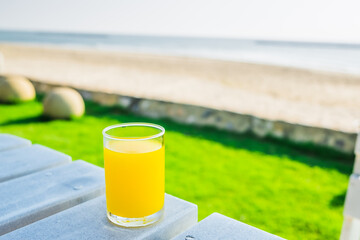 The glass of fresh orange juice on the beach background. The cup of a pure citrus cocktail is organic. Cold beverage for healthy in the tropical summer. Natural food drink squeezed pulp.