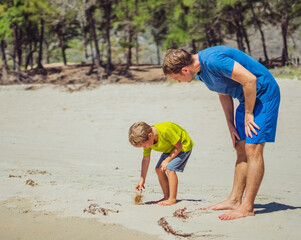 Father son walk on sun sea beach near forest park, study parts of plants on sand. Happy childhood....