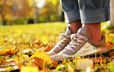 The girl stands in the yellow fallen leaves. In the autumn city park.Autumn women's shoes on the legs of a girl. The girl is wearing blue jeans.