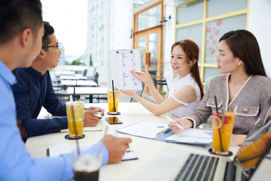 Smiling pretty young Asian businesswoman showing set of charts when sharing her business udeas with colleagues at meeting