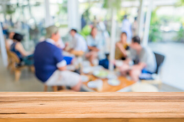 Wood table in front of group young friends come to meet and laughing enjoy in the cafe blur background. Brown wooden desk in front of crowd group talking in coffee shop. Empty counter in restaurant.
