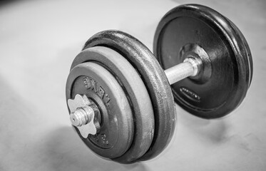 Metal heavy dumbbell on empty floor in the gym. Weight sport for exercise. Fitness or bodybuilding concept background. Monochrome tones