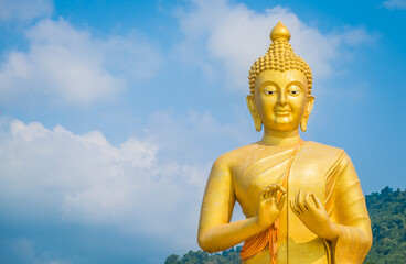 Beautiful golden buddha statue on blue sky background at Makha Bucha Buddhist memorial park, Nakhon Nayok Province, Thailand. Copy space
