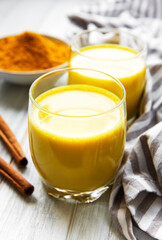Yellow turmeric latte drink. Golden milk with cinnamon, turmeric, ginger  and honey over white marble background.