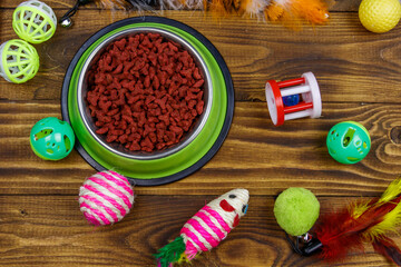Set of toys for cat and bowl with dry pet food on wooden background. Top view. Pet care concept