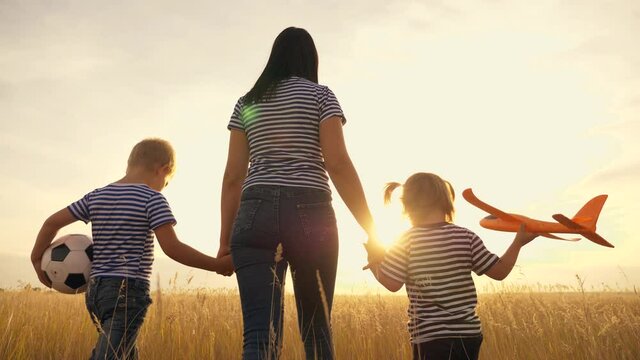 Happy family in the park. Mom and kids are walking in the park at sunset with an airplane and a ball. Kids dream of victories and flights. Dream to be an airplane pilot. Happy family concept. Football