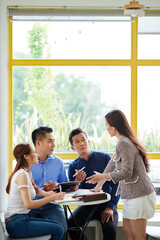 Team of business people sitting at cafe table and looking at female colleague offering new creative ideas for business development