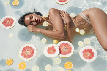 Beautiful Girl's Portrait In Pool With Citrus. Woman In Bikini Enjoying Sunny Day At SPA Resort.