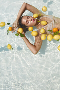 Model's Portrait In Pool With Citrus. Beautiful Girl Floating On Water With Fresh Tropical Fruit At SPA.