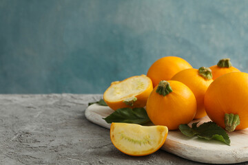 Board with round zucchini and leaves on gray background