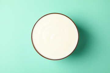 Bowl of sour cream on mint background, top view