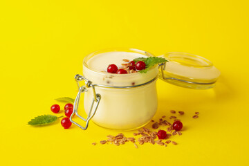 Glass jar of sour cream yogurt with cranberry, mint and granola on yellow background