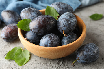 Napkin and bowl with plums on gray background