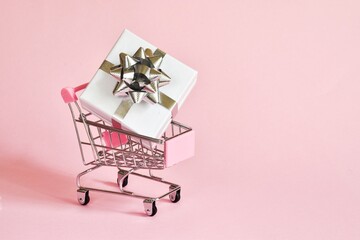 Online shopping concept - full shopping mini cart with white gift box on pink background.