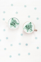 Top view of cup of coffee cappuccino with pattern New Year tree on white wooden table decorated blue snowflakes.
