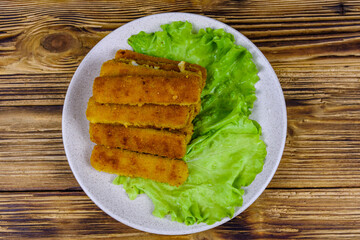 Baked fish sticks and lettuce leaves in a plate. Top view
