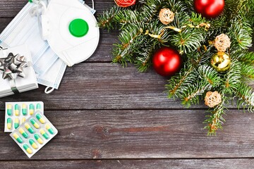 Christmas medicine. New year concept during the covid-19 coronavirus. Top view of electronic thermometer, disposable masks and christmas tree on wooden background. Copy space, flat lay.
